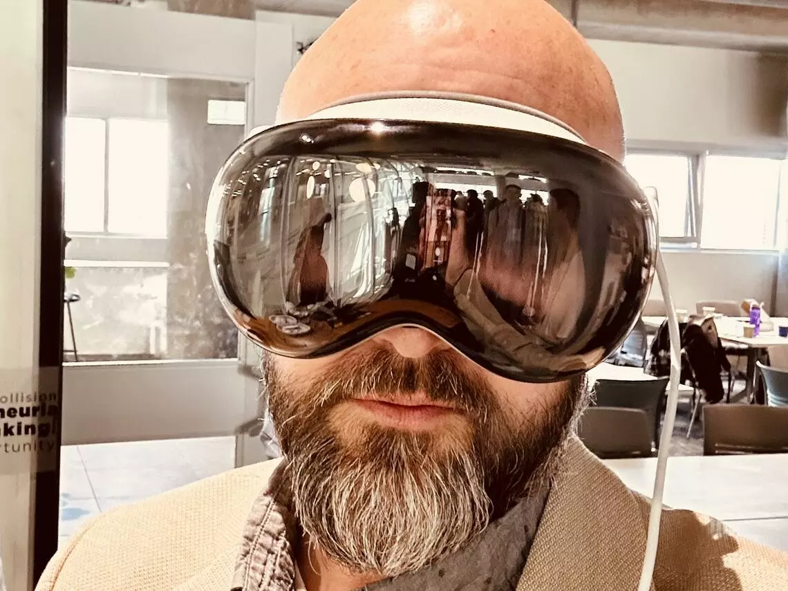 D’Arcy Norman, a bald white man with a beard, wearing virtual reality goggles.